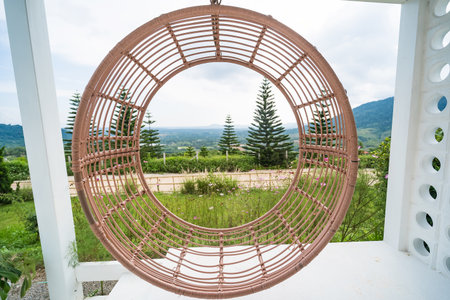 Circular woven hanging chair on a patio with a scenic view of pine trees and rolling hills in the backgroundの写真素材