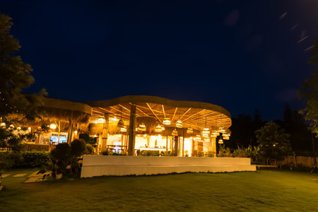 Phetchabun, Thailand - June, 08, 2025 : Cozy outdoor lounge area with woven lampshades and rustic decor under a wooden roof illuminated at night at Phetchabun, Thailandの写真素材