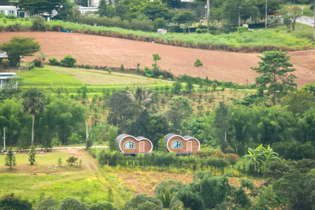 Idyllic countryside scene with lush greenery, trees, small houses, and a tranquil lake reflecting the surrounding landscapeの写真素材
