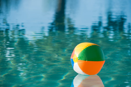 Colorful beach ball floating on a tranquil swimming pool with reflections of trees in the water...