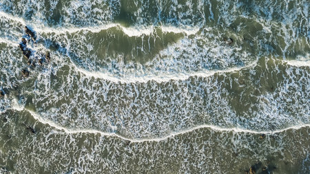 Aerial view of ocean waves crashing onto a rocky coastline with foamy white surf
