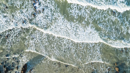 Aerial view of ocean waves crashing onto a rocky coastline with foamy white surf