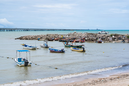 Rayong, Thailand - July, 18, 2025 : Fishing boats moored on a sandy beach near the ocean with a...