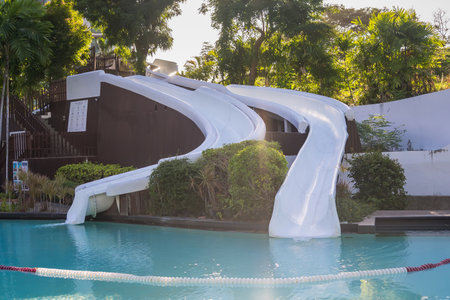 Rayong, Thailand - July, 18, 2025 :White water slide curves into a clear blue swimming pool...