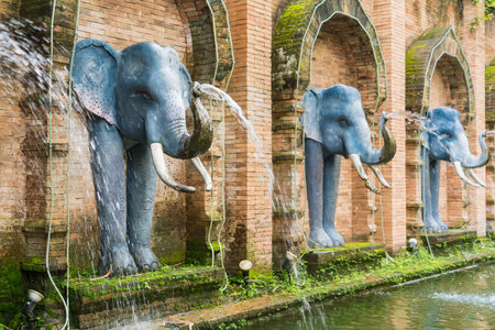 Decorative elephant fountains line a brick wall in a serene garden setting with water gracefully cascading into a tranquil poolの写真素材