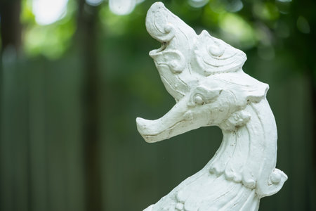Ornate white stone sculpture of mythical bird with foliage backdrop in a lush garden settingの写真素材