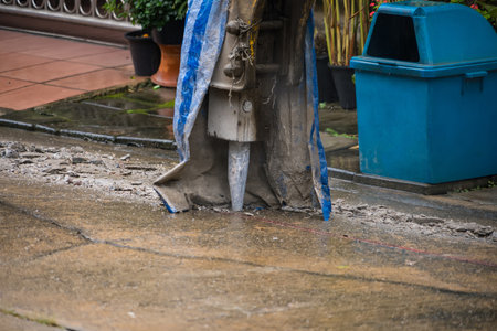 Hydraulic jackhammer drill demolishing concrete on urban street near residential house with potted plants and blue trash bin nearbyの写真素材