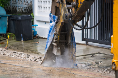 Hydraulic jackhammer on excavator breaking up concrete pavement during road construction work in...