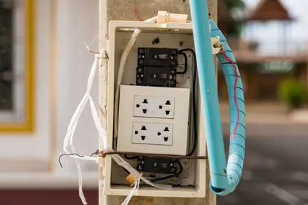 Old damaged electrical switchboard mounted on wall with exposed wiring and multiple power sockets in unsafe conditionの写真素材