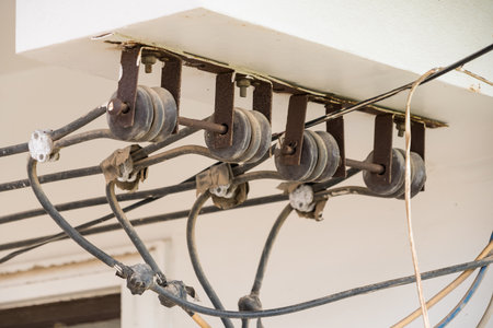 Close-up of multiple old electrical insulators and black power cables mounted on a wall for overhead...
