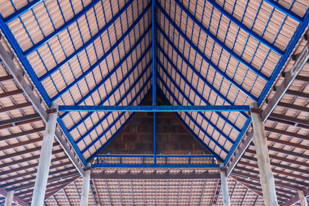 Interior view of a traditional wooden roof structure with exposed beams and blue steel framing supporting clay roof tilesの写真素材