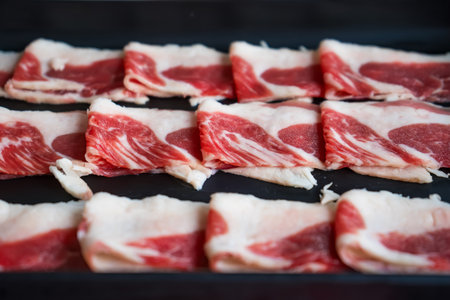 Close-up of raw sliced beef or pork belly meat arranged neatly on a black tray ready for hot pot...