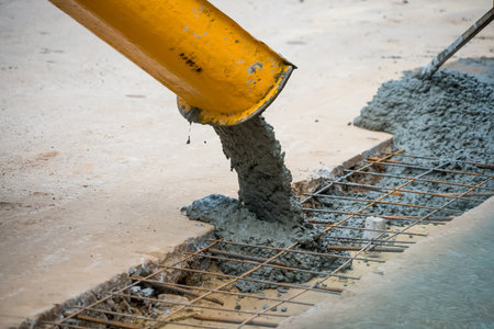 Wet concrete being poured from a yellow chute onto steel reinforcement bars at a construction siteの写真素材