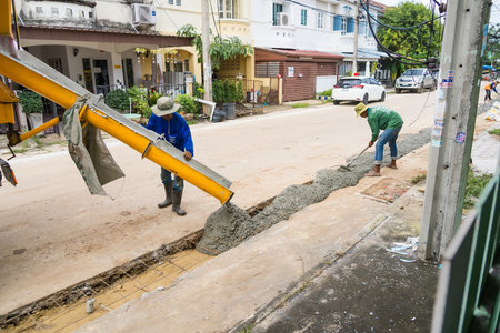 Nonthaburi, Thailand - November, 07, 2025 : Construction workers pouring and spreading concrete from a cement mixer for a new sidewalk on a residential streetの写真素材