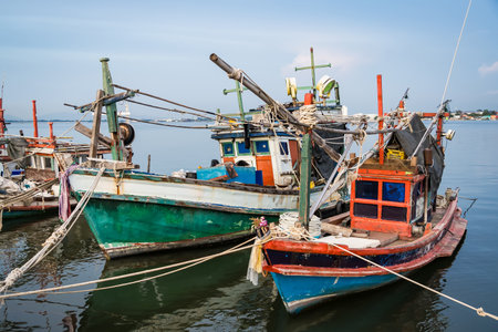Traditional wooden fishing boats docked in a calm harbor with ropes and nets visible during a peaceful seaside dayの写真素材