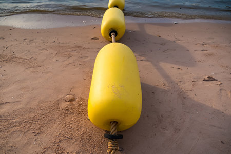 Line of yellow floating buoys forming a barrier in calm blue water with clear sky reflectionの写真素材