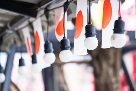 Close-up of hanging light bulbs and Japanese flags used as decorations for a festival or outdoor eventの写真素材