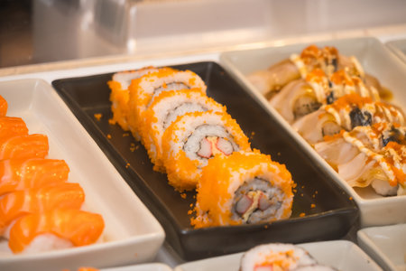 Close-up of assorted sushi rolls on display in a buffet setting including California rolls and various types of nigiriの写真素材