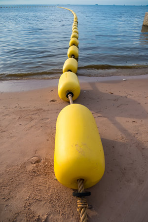 Line of yellow floating buoys forming a barrier in calm blue water with clear sky reflectionの写真素材