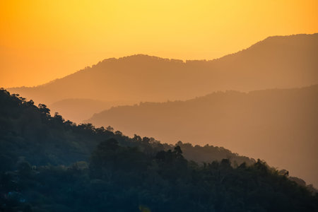 Layered mountain ridges fade into the distance under a warm golden sky at sunrise or sunset with...
