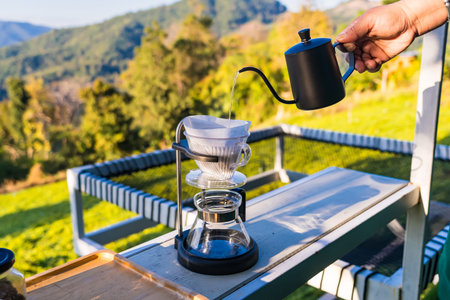 Person brewing fresh coffee outdoors using a pour over method with scenic mountain landscape in the...