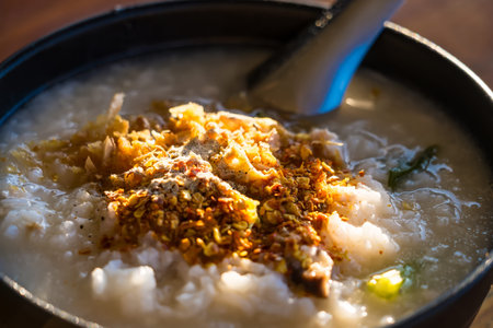Close-up of a bowl of hot rice porridge garnished with spices, herbs, and meat in natural sunlight