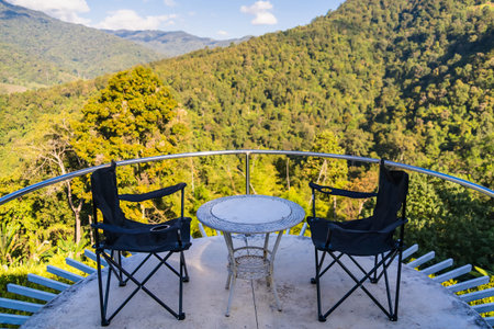 Two camping chairs and a small round table on a balcony overlooking a lush green mountainous forest...