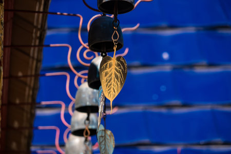 Artistic Wind Chimes in Calmness: An intimate portrayal of hanging wind chimes with gold and silver leaf charms, gently swaying with the breeze, against a calming blue backdrop.の写真素材