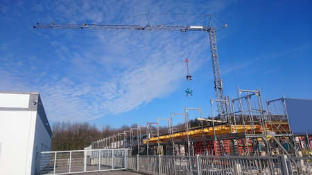 Large construction site with crane on which a cement mixer hangs in bright blue skyの写真素材