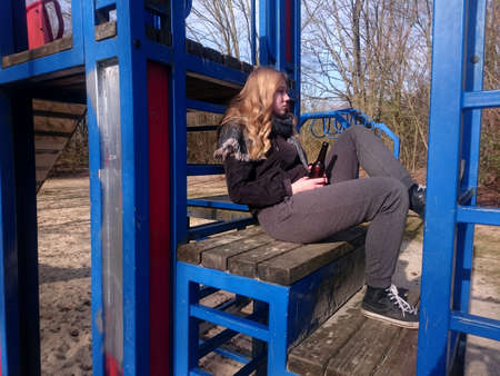 Teenage boy sits with a beer bottle on the climbing frame of a playgroundの写真素材
