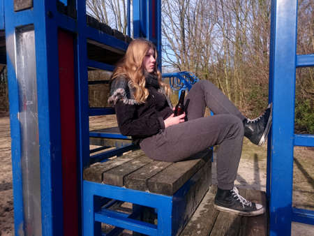 Adolescent with a defiant look sits with a beer bottle a climbing frame of a playgroundの写真素材