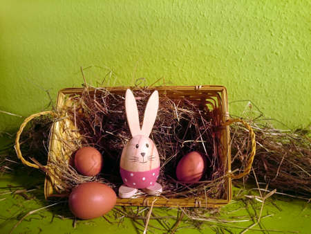 Basket with straw, brown eggs and a decorative rabbit with green backgroundの写真素材