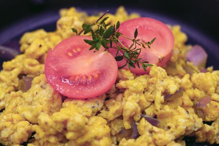 fresh scrambled eggs in pan with tomatoes and herbs in closeup.の写真素材