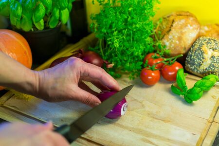 Woman's hand holds red onion on a wooden board to cut it.の写真素材