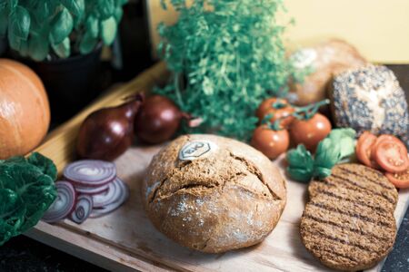 Ingredients for a vegetarian burger lie around an organic bun on a wooden board. In cool colors.の写真素材