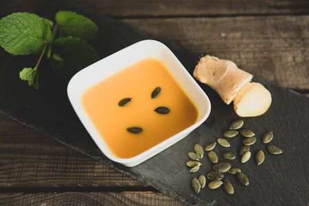 Pumpkin soup with ginger, pumpkin seeds and mint on a slate plateの写真素材