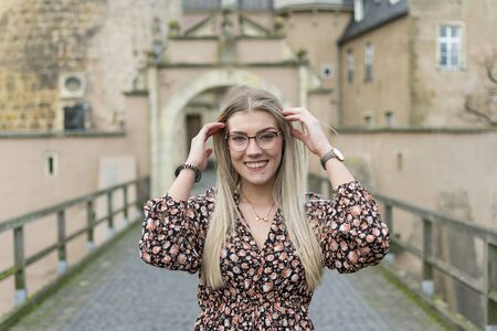 Portrait photo of a laughing young woman with blonde hair and glasses, who runs her hands through her hairの写真素材