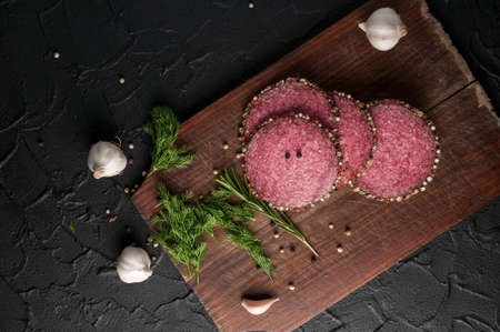 Smoked salami on a black table and brown board. Sausages with rosemary, garlic and pepper and onionsの写真素材