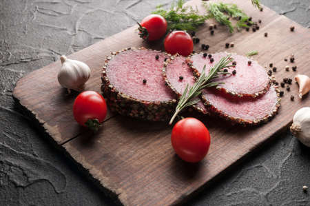 Smoked salami on a black table and a brown board. Sausages with rosemary, garlic and pepper and...