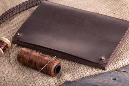 leather dark brown purse on a dark wooden background, with a thread and a needle