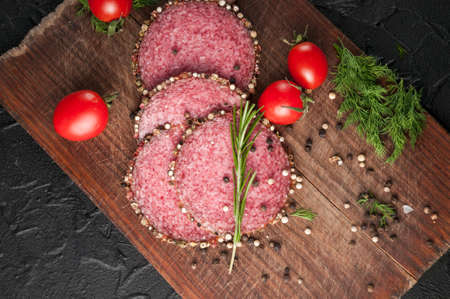 Smoked salami on a black table and a brown board. Sausages with rosemary, garlic and pepper and tomato cherry, dill, parsleyの写真素材