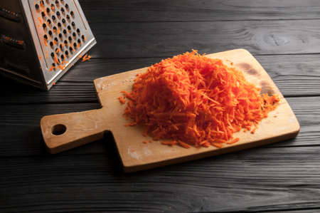 Grated carrots on a blackboard against a wooden background with a metal floatの写真素材