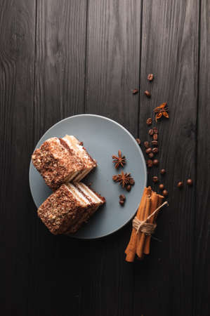 Sweet dessert tiramisu in a cut on a gray plate on a black wooden background with spices: cinnamon sticks and badan, coffee beansの写真素材