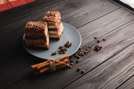 Sweet dessert tiramisu in a cut on a gray plate on a black wooden background with spices: cinnamon sticks and badan, coffee beansの写真素材