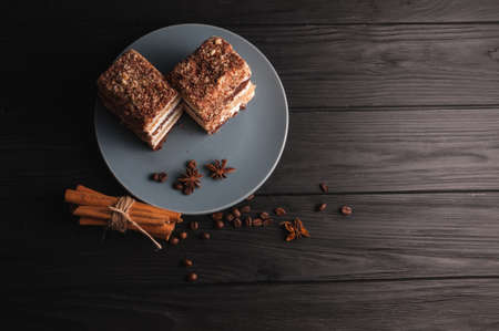 Sweet dessert tiramisu in a cut on a gray plate on a black wooden background with spices: cinnamon sticks and badan, coffee beansの写真素材