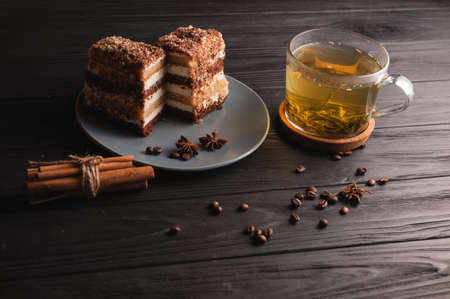 Two pieces of multi-layered honey cake on a plate, on a black wooden background with a cup of tea,...