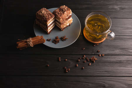 Two pieces of multi-layered honey cake on a plate, on a black wooden background with a cup of tea, chopsticks and coffee grains, top viewの写真素材