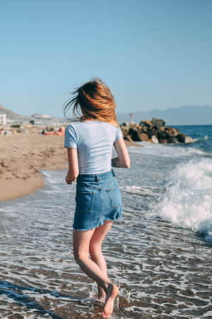 Young girl runs along the sea sandy beach barefoot, concept, view from behindの写真素材