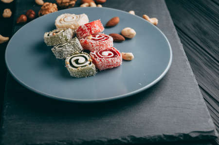 Traditional oriental sweets and nuts: hazelnuts, cashews on a dark wooden background. Turkish dessert is the Rakhat locus. View from above. Place under the textの写真素材