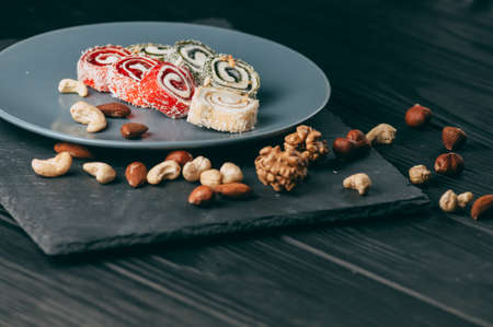Traditional oriental sweets and nuts: hazelnuts, cashews on a dark wooden background. Turkish dessert is the Rakhat locus. View from above. Place under the textの写真素材
